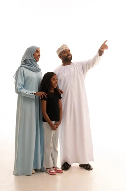 الرعايه والاهتمام بالأبناء، الاشارة الى شيء ما، عائلة عمانية تقضي اوقات ممتعة، النظر إلى الكاميرا بايماءات السعادة والسرور، بورتريه لرجل عربي خليجي عماني يرتدي الدشداشة والكمة يقف مع زوجته وابنته، تعزيز العلاقات الاجتماعية، الجسم بالطول الكامل، خلفية بيضاء
