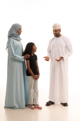 Exchanging entertaining dialogues and discussions, an Omani family spending enjoyable times, caring for and paying attention to children, a portrait of an Arab Gulf Omani man wearing a dishdasha and kumma standing with his wife and daughter with gestures of happiness and joy, enhancing social relationships, full-body, white background.