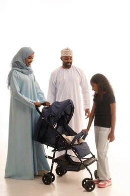 An Omani family spends enjoyable times, going on picnics and family outings, the importance of parents and their essential role in raising and nurturing children, caring for and looking after the kids. A portrait of an Arab Gulf woman from Oman wearing an abaya and hijab standing with her husband and daughter who is pushing a stroller, full-body shot, white background.