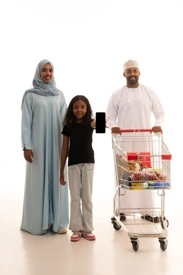 الاستمتاع بالتسوق في المولات والمراكز التجارية، عرض شاشة سوداء عبر الهاتف المحمول، شراء المستلزمات والحاجيات الضرورية، الاستفادة من الخصومات على المنتجات، بورتريه لرجل عربي خليجي عماني يرتدي الدشداشة و الكمة يجرعربة التسوق برفقة زوجته و ابنته، الجسم بالطول الكامل، خلفية بيضاء