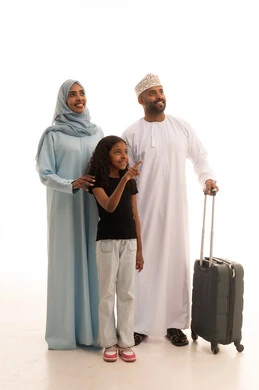 الاشارة الى شيء ما بإيماءات السعادة والسرور، بورتريه لسيدة عربية خليجية عمانية ترتدي العباءة والحجاب تقف مع زوجها و ابنتها بجانب حقيبة الأمتعة، الإستعداد لقضاء الإجازة الصيفية والذهاب في رحلة سفر، الأجواء العائلية المليئة بالحب، الجسم بالطول الكامل، خلفية بيضاء