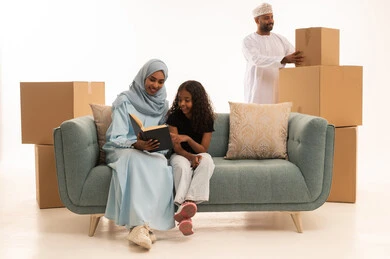 تعزيز الروابط العائلية، صناديق وحاويات كرتونية،  إهتمام الأم بالأبناء ومفهوم السعاده الأسريه، بورترية لإمرأة عربيه خليجيه عمانية محجبة تجلس على  الاريكة تقوم بقراءة القصص المسليه لابنتها، الإستمتاع بالأنشطه الترفيهية وقضاء الوقت مع الاولاد، خلفية بيضاء