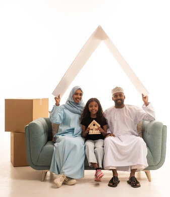 مفهوم امتلاك سكن جديد والاستقرار العائلي، صناديق وحاويات كرتونية، زوجان عربيان خليجيان عمانيان يجلسان على الايكة برفقه ابنتهم يحملان لوح ابيض فوق راسهم، بورتريه لعائلة عربية خليجية عمانية ، بنت تمسك بيديها مجسم بيت صغير، ايماءات وجه ويدين تدل على السعادة، خلفية بيضاء