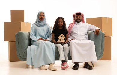 A girl holding a model of a small house, owning a new home, boxes and cardboard containers, a portrait of a Saudi Arabian Gulf family wearing traditional attire sitting on the sofa looking at the camera with expressions of happiness and joy, moving furniture to a new house, white background.