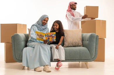 الاهتمام بتعليم الأبناء ودعمهم، بورتريه لام عربية سعودية خليجية ترتدي عباءة تجلس على الاريكة تقوم بتدريس ابنتها، المساعدة في تأدية الواجبات المدرسية، الانشطة التعليمية وتنمية القدرات، صناديق وحاويات كرتونية، مفهموم امتلاك سكن جديد والاستقرار العائلي خلفية بيضاء