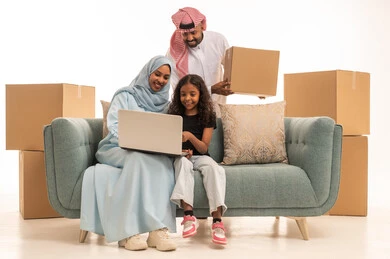 حل الواجبات المنزليه، دمج التعليم مع التقنية و التكنولوجيا، صناديق وحاويات كرتونية، متابعة منصات التعليم الالكتروني المتاحة عبر الانترنت، بورتريه لأم عربية خليجة سعودية محجبة تجلس على الاريكة تقوم بتعليم وتدريس ابنتها باستخدام الحاسب المحمول برفقة زوجها، خلفية بيضاء