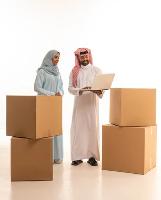 التأكد من خدمة شحن وتوصيل البضائع، الانتفال الى منزل جديد، بورتريه لزوجان خليجيان سعوديان عربيان يستخدمان الحاسوب المحمول، اجراء طلبات أونلاين، امتلاك سكن جديد والاستقرار العائلي، استخدام تقنيات حديثة، الجسم بالطول الكامل، خلفية بيضاء