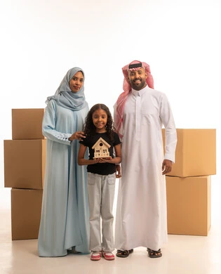 امتلاك سكن جديد، صناديق وحاويات كرتونية، بنت تحمل مجسم لبيت صغير، بورتريه لعائلة عربية خليجيه سعودية ترتدي الزي التقليدي تنظر الى الكاميرا بتعابير السعادة و السرور، نقل العفش لبيت جديد، العمل الجماعي الأسري، الجسم بالطول الكامل، خلفية بيضاء