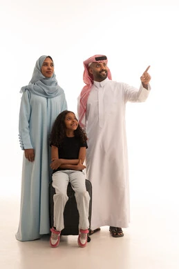 الاستعداد لقضاء العطلة الصيفية، الاشارة الى شيء ما ، بورتريه لعائلة عربية خليجية سعودية مبتسمة وسعيدة مستعدة للسفر ، بنت عربية خليجيه سعودية ترتدي الزي الكاجوال تجلس على حقيبة السفر ، مفهوم السياحة وسفر ، الاستمتاع بوقت ممتع مع العائلة ، الجسم بالطول الكامل، خلفية بيضاء