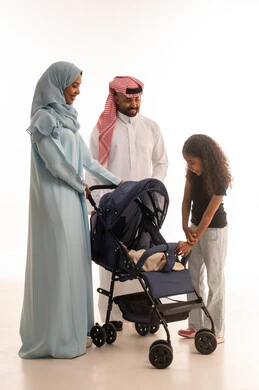 الرعاية والاهتمام بالأولاد, أهمية الأهل ودورهم الأساسي في تربية الأبناء, بورتريه لسيدة عربية خليجية سعودية ترتدي الحجاب والعباءة تقف مع زوجها وابنتها تقوم بجر عربة الطفل، القيام بنزهة وجولة عائلية، عائلة سعودية تقضي وقت ممتع، الجسم بالطول الكامل، خلفية بيضاء