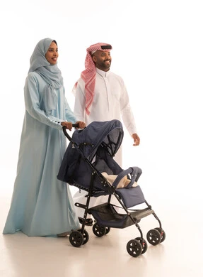 عائلة سعودية تقضي اوقات ممتعة، القيام بالنزهات والجولات العائلية، الرعايه والاهتمام بالأولاد, أهمية الأهل ودورهم الأساسي في تربية ونشأة الأبناء, بورتريه لرجل عربي خليجي سعودي يرتدي الثوب التقليدي و الشماغ  يقف مع زوجته ويقوم بجرعربة الأطفال، خلفية بيضاء