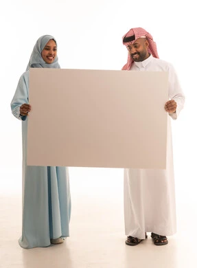 استخدام لوحات توضيحية ووسائل تعليمية، إعلانات وعروض تسويقية، بورتريه لرجل عربي خليجي سعودي يرتدي  الثوب التقليدي و الشماغ يحمل بيده لوح ابيض كبير (موك اب فارغ) برفقة زوجته ، ايماءات السعادة والسرور، الطول الكامل للجسم، خلفية بيضاء