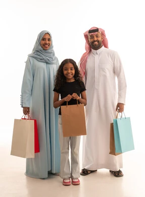 الاستمتاع بالشراء وتبضع الأغراض خلال الجمعة البيضاء، تسوق المنتجات العالمية والسعودية، بورتريه لزوجان عربيان خليجيان سعوديان يحملان أكياس التسوق الملونة برفقة ابنتهم ، استغلال التخفيضات والعروض الموسمية، الطول الكامل للجسم، خلفية بيضاء