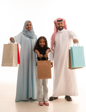 Shopping for global and Saudi products, enjoying shopping and buying items during Black Friday, a portrait of an Arab Gulf couple from Saudi Arabia carrying colorful shopping bags with their daughter, taking advantage of discounts and seasonal offers, full body length, white background.