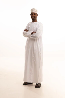 Standing with crossed arms, paying attention to appearance and elegance, the concept of masculinity and self-confidence, a portrait of a young Arab Gulf Omani man with a dark complexion wearing a dishdasha and a kumma, looking with expressions of joy, full-body image, white background.