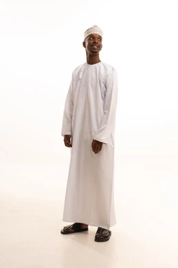 Attention to appearance and elegance, the concept of masculinity and self-confidence, a portrait of a young Arab Gulf Omani man with a dark complexion wearing a dishdasha and kumma, looking with expressions of joy, standing upright and steady, full-body image, white background.
