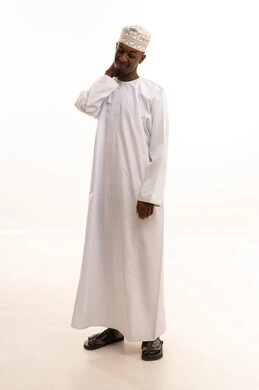 Neck, bone, and spine pain, gestures of distress and suffering, a portrait of a young Arab Gulf Omani man with a dark complexion wearing a dishdasha and kumma, holding his neck with gestures of pain, the necessity of going to the doctor and getting treatment, white background.