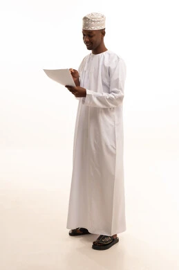 Preparing work-related reports, checking the reading of notes, a portrait of a young Arab Gulf Omani man with a dark complexion wearing a dishdasha and kumma holding a set of white papers in his hand, reviewing and following up on office plans and projects with focused gestures, white background.