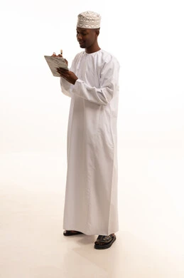 تدوين وتسجيل الملاحظات والمعلومات على الورق, تنظيم وإدارة الأعمال ،  بورتريه لشاب عربي خليجي عماني اسمر يرتدي الدشداشة والكمة يقوم بكتابة المهام والأهداف اليومية, خلفية بيضاء