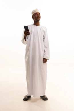 Making a phone call, using modern technologies, browsing social media sites via mobile, completing work tasks remotely, a portrait of a young Arab Gulf Omani man with a dark complexion wearing a dishdasha and kumma using a mobile phone, white background.