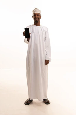 Making a phone call, using modern technologies, browsing social media sites via mobile, completing work tasks remotely, a portrait of a young Arab Gulf Omani man with a dark complexion wearing a dishdasha and kumma using a mobile phone, white background.