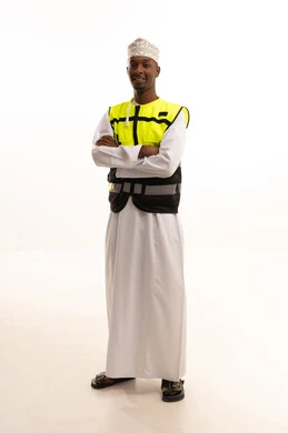 Working in the engineering sector, the concept of engineering and architectural constructions, a portrait of a young Arab Gulf Omani man with a dark complexion wearing a dishdasha, a kumma, a helmet, and a safety vest, looking with gestures of joy, Omani professions and jobs, construction with the hands of the nation's sons, white background.