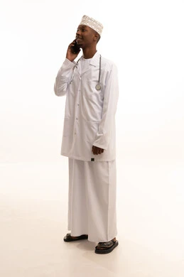 اجراء الاستشارات الطبيه عن بعد، اجراء مكالمة هاتفية ، استخدام التكنولوجيا في البحث والتطوير، تقديم الخدمات للمرضى بكل كفاءه،بورتريه لشاب عربي خليجي عماني اسمر يرتدي الدشداشة والكمة مع المعطف الابيض يستخدم الهاتف المحمول، مهن ووظائف صحية، خلفيه بيضاء