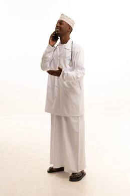Making a phone call, using technology in research and development, providing services to patients efficiently, conducting telemedicine consultations, a portrait of a young Arab Gulf Omani man with a dark complexion wearing a dishdasha and kumma with a white coat using a mobile phone, health professions and jobs, white background.