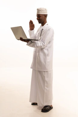 تقديم الخدمات للمرضى بكل كفاءه، استخدام التكنولوجيا في البحث والتطوير،اجراء الاستشارات الطبيه عن بعد، بورتريه لشاب عربي خليجي عماني اسمر يرتدي الدشداشة والكمة مع المعطف الابيض يعمل على جهاز الحاسوب المحمول، مهن ووظائف صحية، خلفيه بيضاء