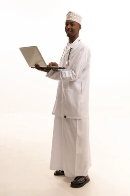 استخدام التكنولوجيا في البحث والتطوير، تقديم الخدمات للمرضى بكل كفاءه، اجراء الاستشارات الطبيه عن بعد، بورتريه لشاب عربي خليجي عماني اسمر يرتدي الدشداشة والكمة مع المعطف الابيض يعمل على جهاز الحاسوب المحمول، مهن ووظائف صحية، خلفيه بيضاء