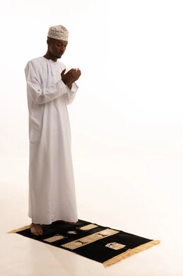 الدعاء والتضرع الى الله، الركوع والسجود والخشوع لله، بورتريه لشاب عربي عماني خليجي اسمر يرتدي الدشداشة والكمة يقف على السجادة و يؤدي فريضة الصلاة ، آداء صلاة التراويح ،أذكار وأدعية وفرائض، خلفية بيضاء.