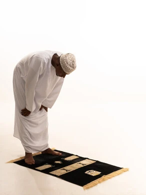 آداء صلاة التراويح ،  الركوع والسجود والخشوع لله، بورتريه لشاب عربي عماني خليجي اسمر يرتدي الدشداشة والكمة يقف على السجادة و يؤدي فريضة الصلاة ، الدعاء والتضرع الى الله، أذكار وأدعية وفرائض، خلفية بيضاء.