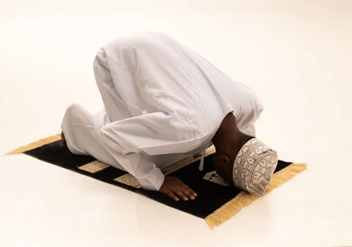 ايماءات التضرع والخشوع ، بورتريه لشاب عربي عماني خليجي اسمر  يرتدي الدشداشة والكمة يقف على السجادة و يؤدي فريضة الصلاة ، آداء صلاة التراويح ، الدعاء الى الله، أذكار وأدعية وفرائض، خلفية بيضاء.