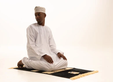 أذكار وأدعية وفرائض، الركوع والسجود والخشوع لله، بورتريه لشاب عربي عماني خليجي اسمر يرتدي الدشداشة والكمة يقف على السجادة و يؤدي فريضة الصلاة ، آداء صلاة التراويح ، الدعاء والتضرع الى الله، خلفية بيضاء.