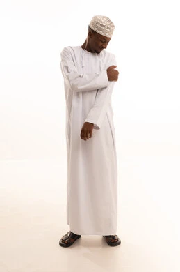 Nerve and muscle pains, seeking help and the need for treatment, inflammation of muscles and joints, a portrait of a dark-skinned Omani Gulf Arab man wearing a dishdasha and turban, placing his hand on his shoulder with gestures of pain, fatigue, and exhaustion, an emergency medical condition, full-body image, white background.