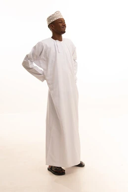 The sensation of pain and suffering from disc disease, back pain, spinal pain, and arthritis, a portrait of a young Arab Gulf Omani man with a dark complexion wearing a dishdasha and a kumma, standing with difficulty and holding his back with his hands in gestures of suffering, white background.