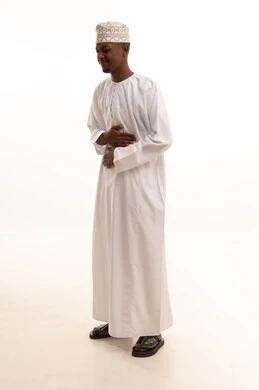 أمراض والتهابات الجهاز الهضمي، المعاناة من آلام البطن والمعدة، الحاجة إلى العلاج، بورتريه لشاب عربي خليجي عماني اسمر  يرتدي الدشداشة والكمة يضع يديه على بطنه بتعابير التعب والإرهاق والإحساس بالمرض، خلفية بيضاء