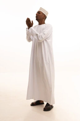 Supplication to Allah the Exalted, the request with hope and humility from the Lord of the servants, a portrait of a young Arab Gulf Omani man with a dark complexion wearing a dishdasha and a kumma, raising his hands in reverence and pleading, seeking help and desiring to fulfill wishes, standing with gestures of prayer, supplication, and seeking mercy, with a white background.