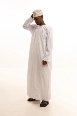 The regret of losing something valuable, the frustration and sadness over missed opportunities, disappointment and experiencing betrayal and shock, a portrait of a young Arab Gulf Omani man with a dark complexion wearing a dishdasha and kumma, placing his hands on his head with expressions of sorrow and regret, white background.