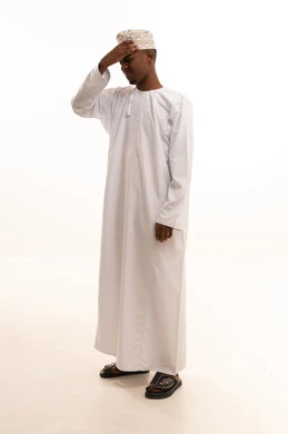 Frustration and sadness over the lost opportunity, disappointment and exposure to betrayal and shock, regret over the loss of something valuable, a portrait of a young Arab Gulf Omani man with a dark complexion wearing a dishdasha and kumma, placing his hands on his head with expressions of sorrow and regret, white background.