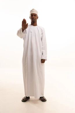 التوقف عن الكلام وخفض الصوت، الهدوء والسكون وعدم الإزعاج، بورتريه لشاب عربي خليجي عماني اسمر يرتدي الدشداشة والكمة يضع يده على فمه بإيماءات طلب السكوت والصمت،خلفية بيضاء