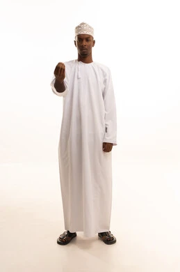 The concept of patience, deliberation, and caution, the threat and promise of something, a portrait of a young Arab Gulf Omani man with a dark complexion wearing a dishdasha and a kumma looking at the camera, raising his hand upwards with gestures asking for patience, white background.