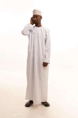 الانصات وحسن الاستماع، بورتريه لشاب عربي خليجي عماني اسمر يرتدي الدشداشة والكمة يضع يده خلف أذنه بإيماءات التنصت والتجسس، التركيز على الكلام وسماع الاسرار، خلفية بيضاء