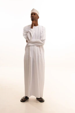 مفهوم الاستماع والتركيز، التطلع والتخطيط للمستقبل، حل المشكلات واتخاذ القرارات،بورتريه لشاب عربي خليجي عماني اسمر يرتدي الدشداشة والكمة يضع يده على ذقنه بإيماءات التفكير وشرود الذهن، خلفية بيضاء