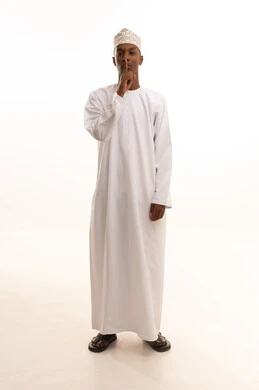 الهدوء والسكون وعدم الإزعاج، التوقف عن الكلام وخفض الصوت، بورتريه لشاب عربي خليجي عماني اسمر يرتدي الدشداشة والكمة  يضع أصبع السبابة على فمه بإيماءات طلب السكوت والصمت،خلفية بيضاء