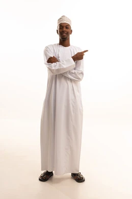 شد الإنتباه ولفت النظر، الإشارة والتوجيه إلى مكان ما، بورتريه لشاب عربي خليجي عماني اسمر يرتدي الدشداشة والكمة يشير بإصبع السبابة إلى شيء ما ينظر بإيماءات السعادة والثقة بالنفس، تحديد موقع أو هدف معين، الجسم بالطول الكامل، خلفية بيضاء