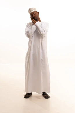 تعابير النعاس والحاجه الى النوم،بورتريه لشاب عربي خليجي عماني اسمر يرتدي الدشداشة والكمة يرفع يديه بإيماءات النعاس, الإحساس بالتعب والتثاؤب ,مفهوم الكسل والخمول، خلفيه بيضاء