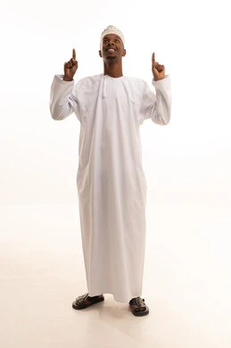 Pointing and directing to a place, attracting attention and drawing notice, a portrait of a young Arab Gulf Saudi man with a dark complexion wearing a white thobe, pointing with his index finger to something, looking with gestures of happiness and self-confidence, identifying a specific location or goal, full-body, white background.