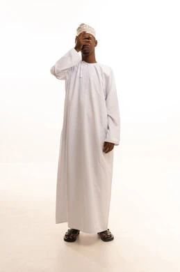 The concept of vision assessment, testing and examining visual acuity, a portrait of a young Arab Gulf Omani man with a dark complexion wearing a dishdasha and kumma, placing his hand over his eye, gestures for eye examination, white background.