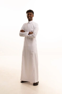 الوقوف بايدي متقاطعة، الاهتمام بالمظهر الخارجي والأناقة، مفهوم الرجولة والثقة بالنفس،بورتريه لشاب عربي خليجي سعودي اسمر يرتدي الثوب الابيض ينظر بتعابير السرور، صورة الجسم بالطول الكامل، خلفية بيضاء